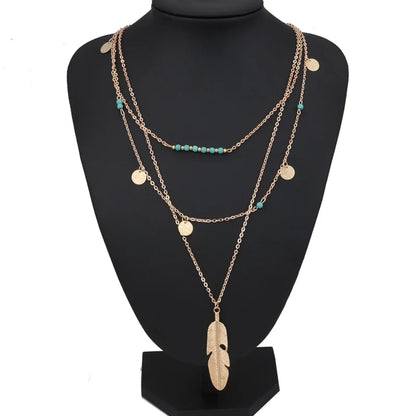 Gold-colored multilayer chain necklace with turquoise beads, coin charms, and a feather pendant.