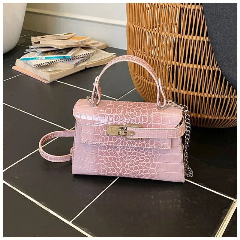 Pink faux leather structured crossbody bag with zip closure and adjustable strap for carrying baby essentials.