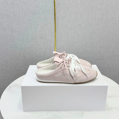 Pink suede backless slip-on loafers with round toes, white laces, and flat soles.