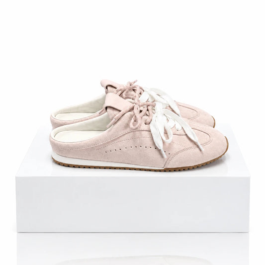 Light pink suede backless sneaker mules with white laces displayed on a white block.