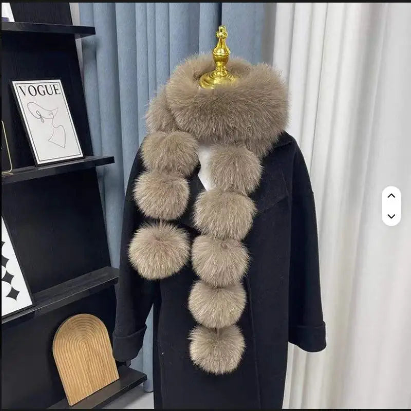 Taupe faux fox fur scarf with multiple dangling pom-poms, displayed on a black coat.
