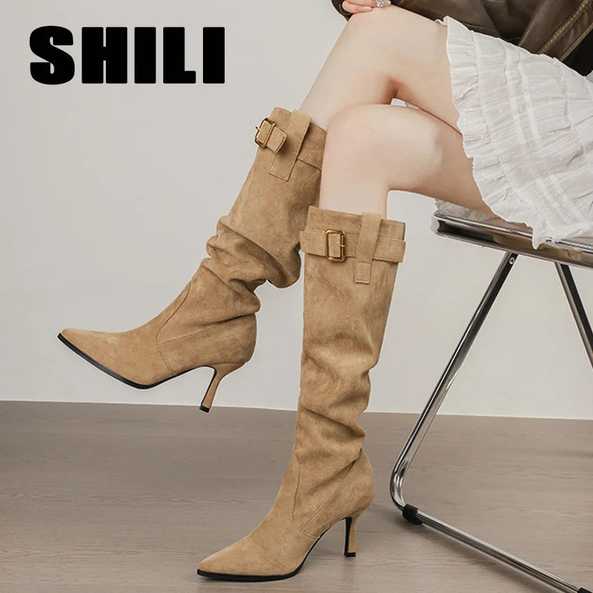 Beige suede knee-high boots with pointed toes, thin high heels, and buckled straps at the collar.