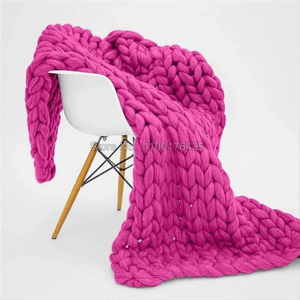 Bright pink chunky knit yarn blanket draped over a modern white chair with wooden legs.