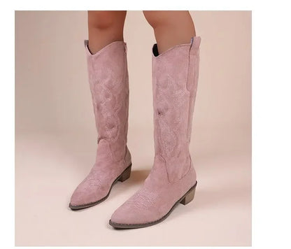 Pink suede western cowboy boots with pointed toes, block heels, and white embroidered shafts.