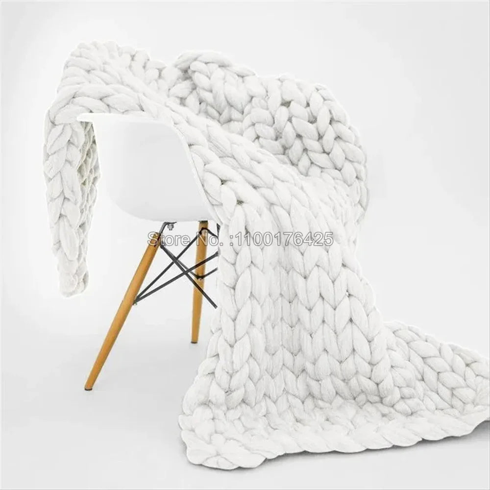 Light grey chunky knit blanket draped over a modern white chair with wooden legs.