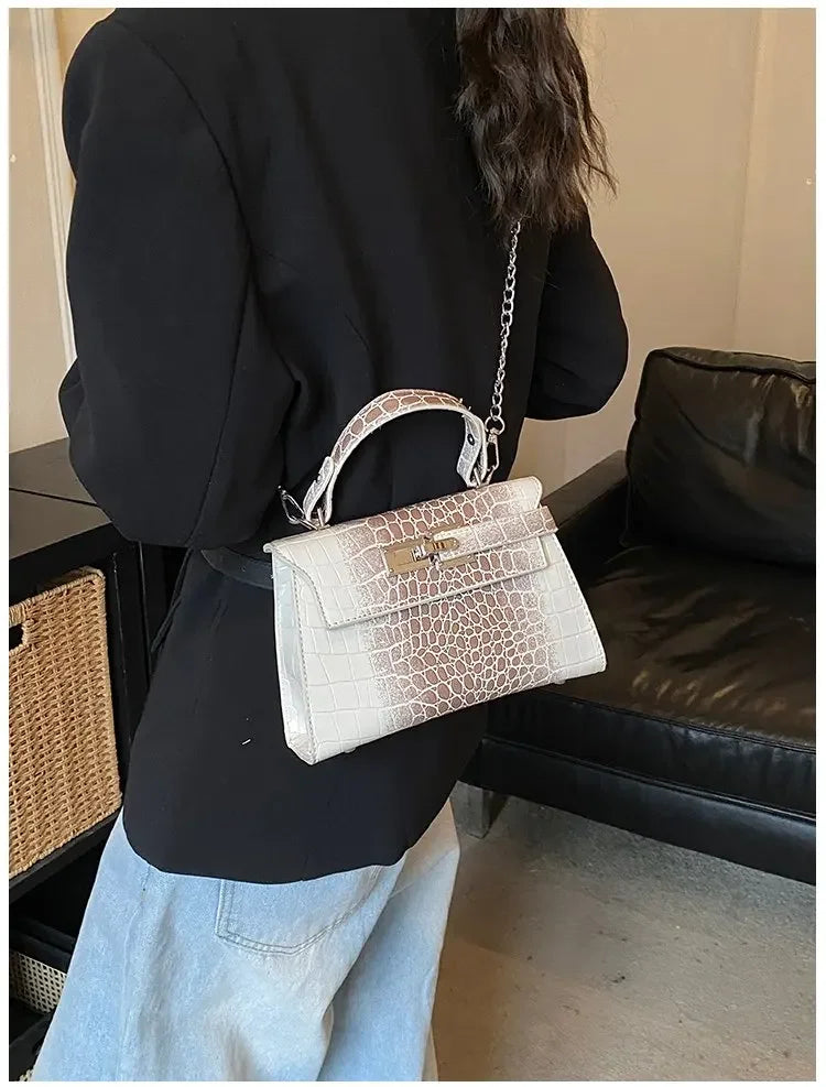 White faux leather crossbody diaper bag with crocodile texture, structured shape, and metal lock for parents on the go.