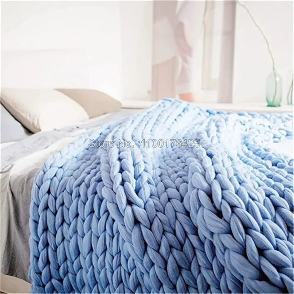 Light blue chunky hand-knitted yarn throw blanket draped over a bed.