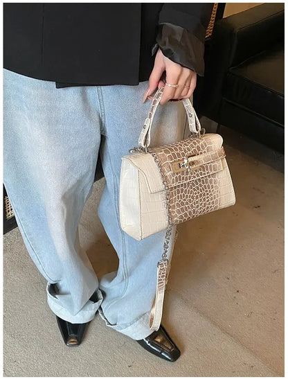 Beige faux leather crossbody satchel with croc-embossed texture, silver hardware, and adjustable strap for baby essentials.