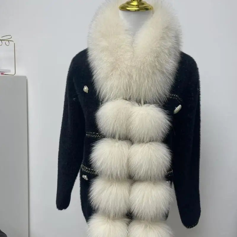 White long faux fox fur scarf with fluffy pom-poms draped over a black cardigan.