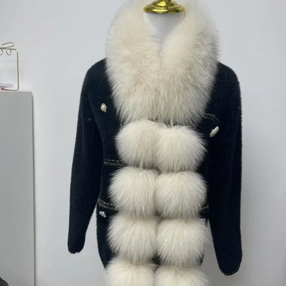 White long faux fox fur scarf with fluffy pom-poms draped over a black cardigan.