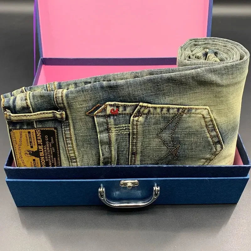 Folded blue denim tapered jeans with a leather patch in a blue box for daily wear.