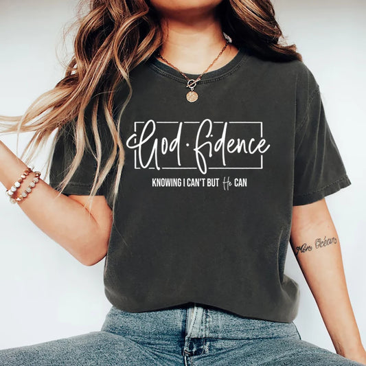 Dark grey t-shirt with white Godfidence text and rectangular outline, and Knowing I Can't But He Can text below.