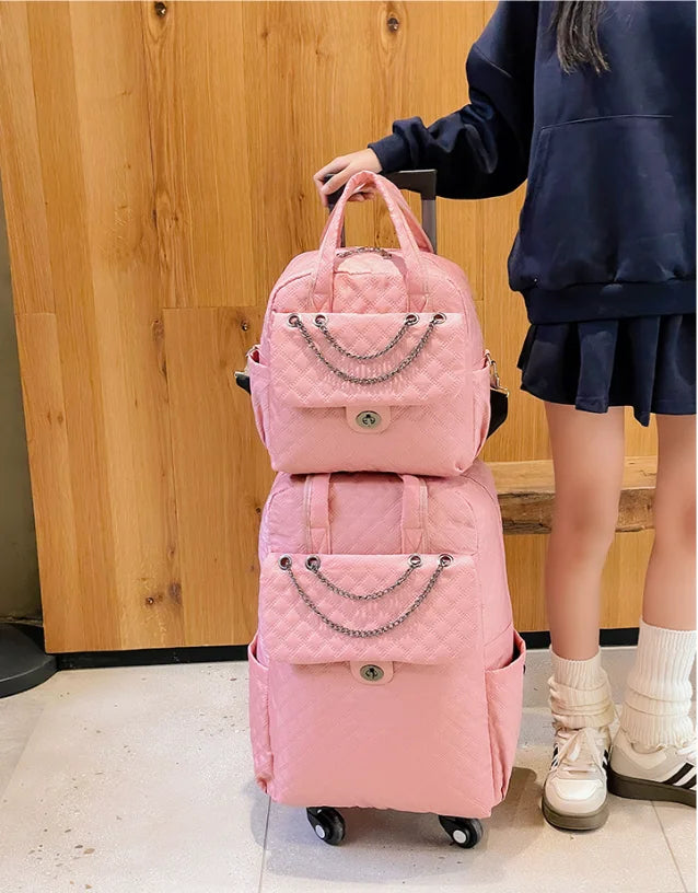 Pink quilted nylon rolling luggage set with chain accent on the front pocket and top handles.