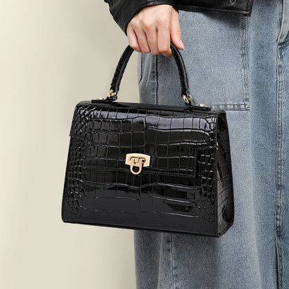 Black leather handbag with glossy crocodile pattern, top handle, flap closure, and gold-tone clasp hardware.
