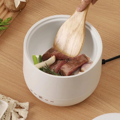 White electric multi-cooker with meat, vegetables, and wooden spatula inside.