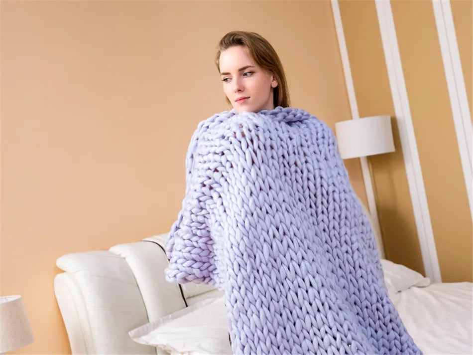 A light purple chunky hand-knit yarn blanket draped around a person in a bedroom.