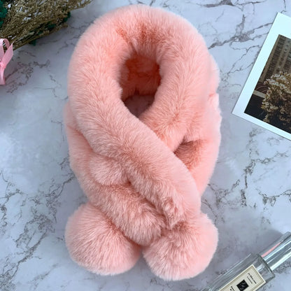 Pink plush faux fur cross scarf with two pom-pom ends on a marble surface.