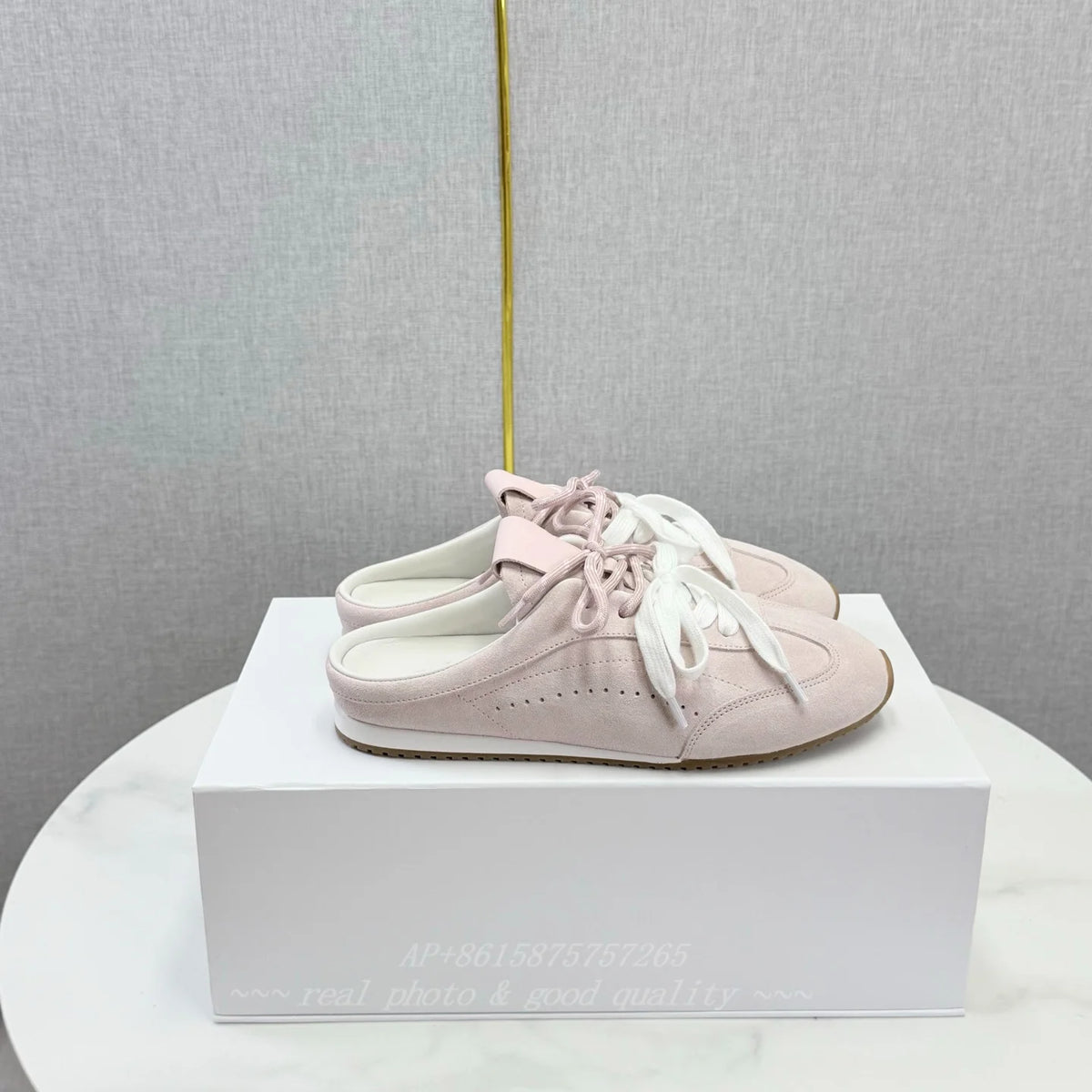 Light pink suede slip-on sneakers with round toes, white laces, and flat soles, resting on a white box.