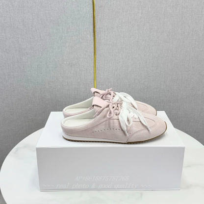 Light pink suede slip-on sneakers with round toes, white laces, and flat soles, resting on a white box.