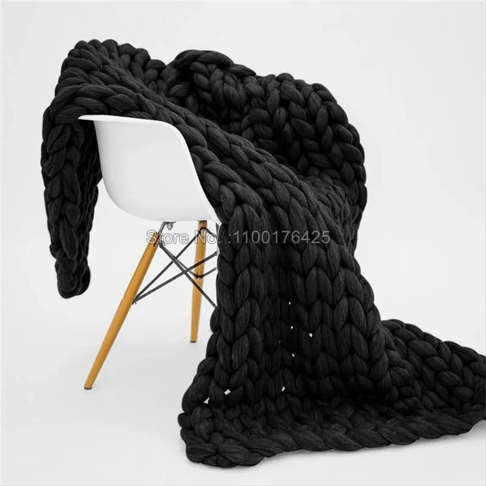 Dark grey, chunky hand-knitted yarn blanket draped over a modern white chair with wooden legs.