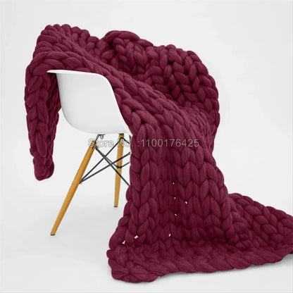 Maroon chunky knit blanket draped over a modern white chair with wooden legs.