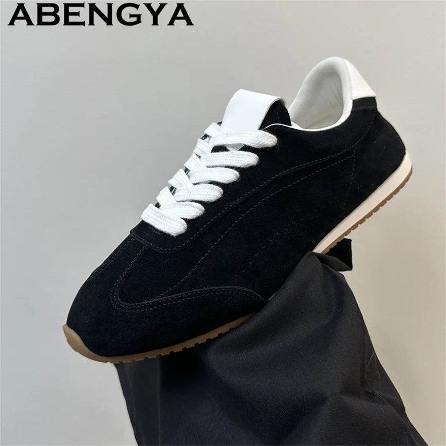 Black suede casual sneaker with white laces, tongue, and heel collar, plus a thin brown rubber sole.