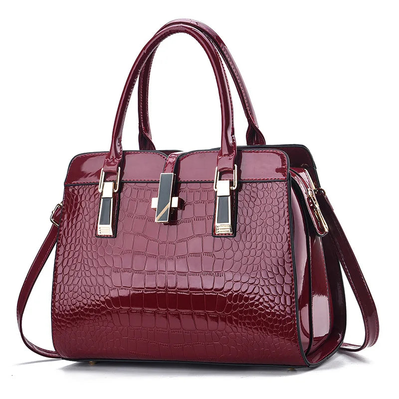 Burgundy patent leather crocodile-pattern handbag with dual top handles and gold hardware accents.
