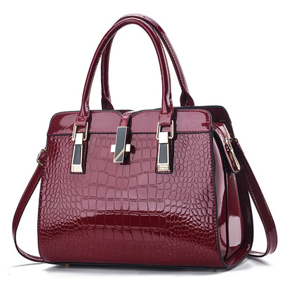 Burgundy patent leather crocodile-pattern handbag with dual top handles and gold hardware accents.