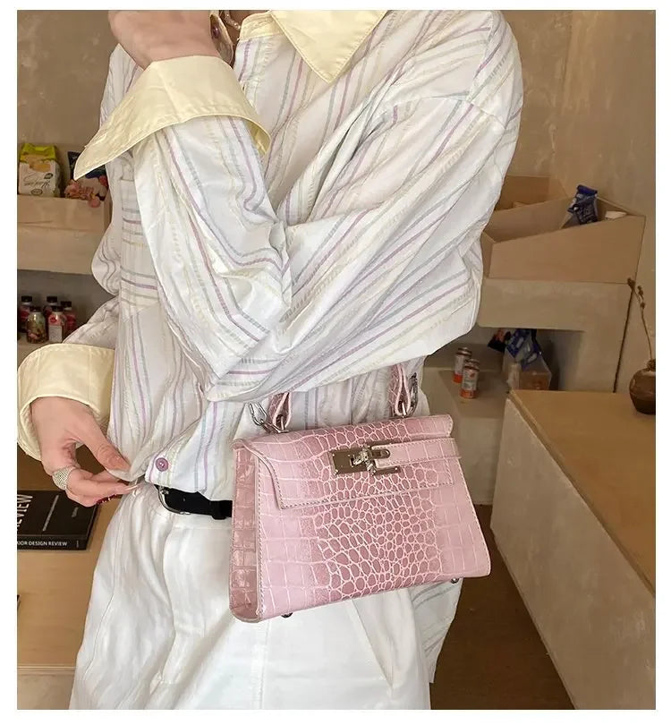 Light pink faux leather structured diaper bag with crocodile texture, metal closure, and handle for baby essentials.