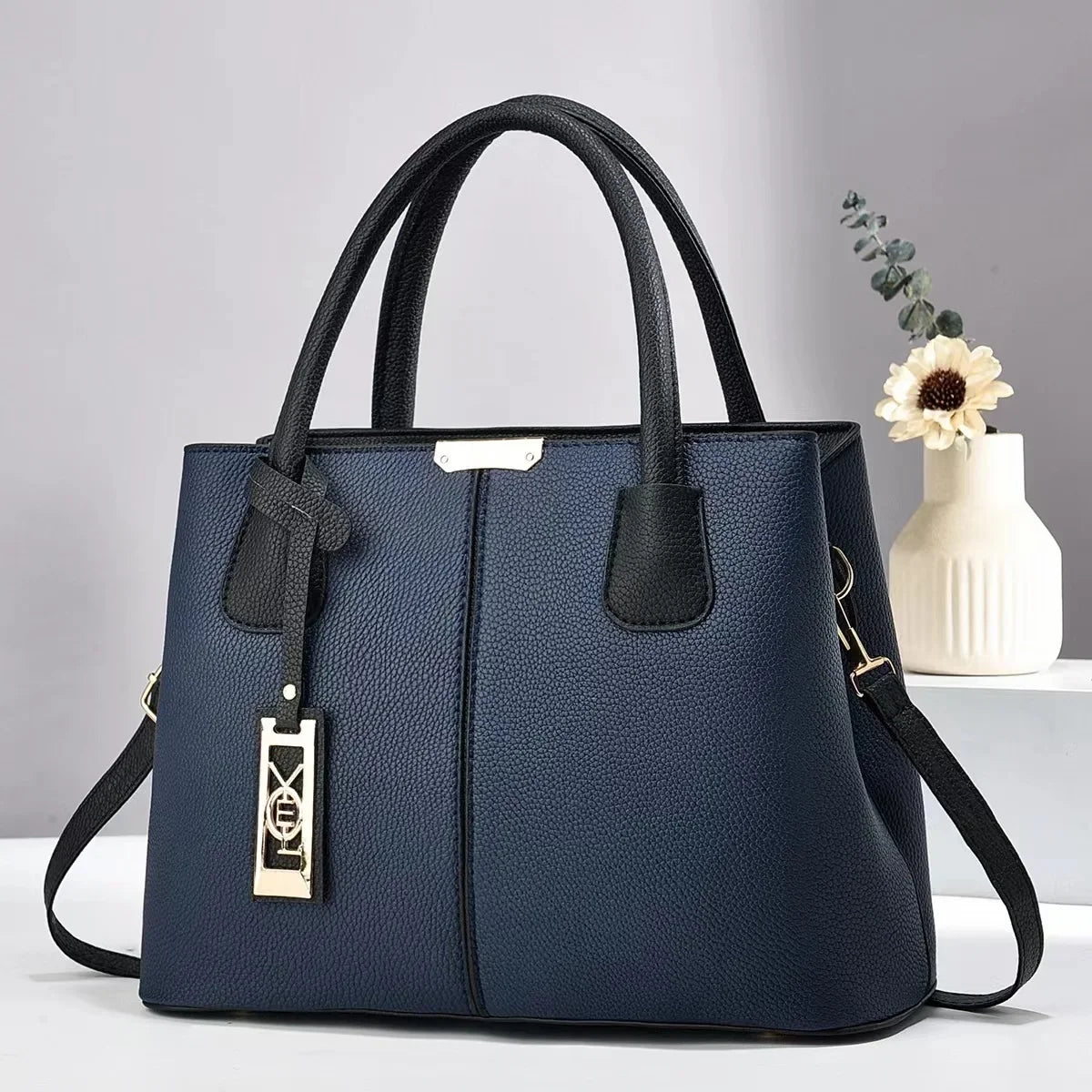 Navy blue faux leather structured tote bag with black handles, gold charm, and zip closure for everyday use.