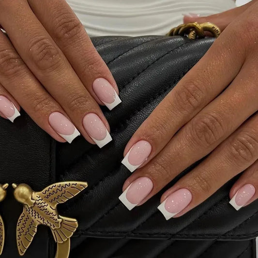 Hands wearing square press-on nails with white tips on a black bag with gold bird charm