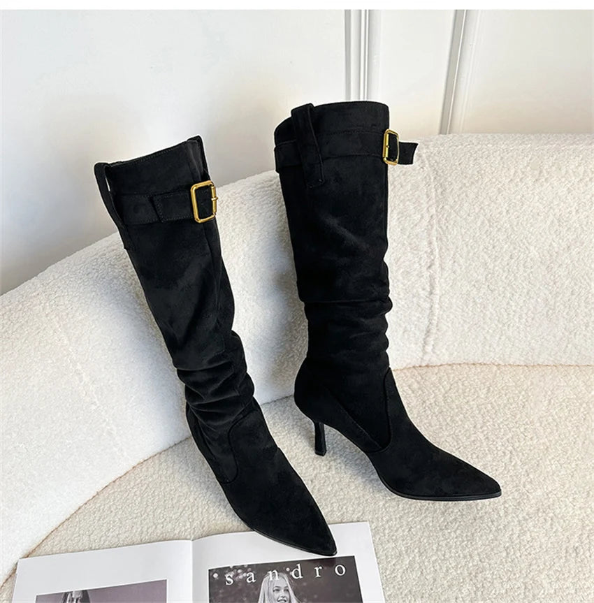 Black suede knee-high boots with pointed toes, thin heels, and gold-buckled ankle straps.