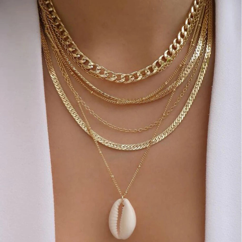 Gold-tone layered chain necklace set with a white cowrie shell pendant for a bohemian jewelry accessory look.