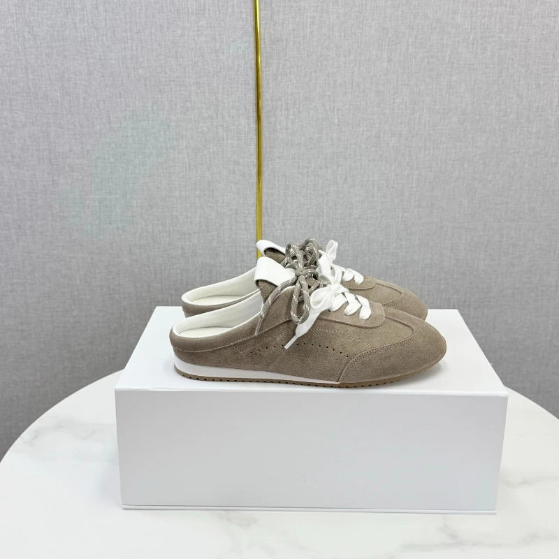 Taupe suede slip-on sneakers with round toes, white laces, and a backless mule design.