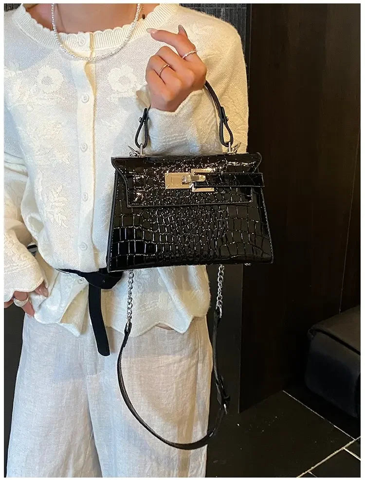 Black faux leather structured diaper bag with crocodile texture, silver metal clasp, and adjustable strap for outings.