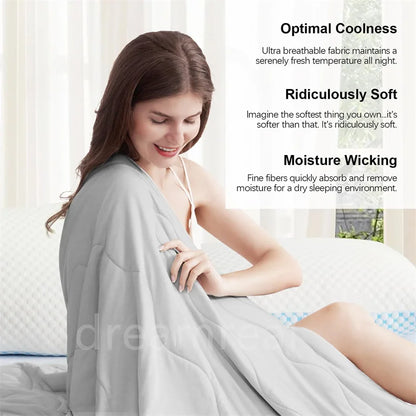 Woman sitting on bed with a light grey, breathable cooling comforter to stay comfortable while sleeping.