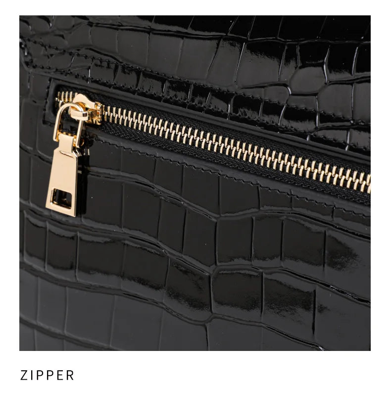 Black patent leather handbag with crocodile pattern, featuring a gold zipper and pull tab.