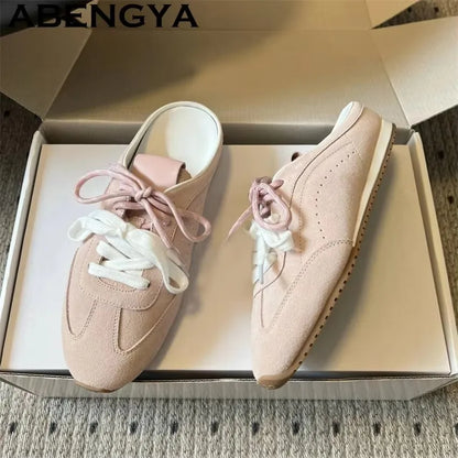 Pink suede slip-on sneakers with white laces and flat soles, in a shoebox.