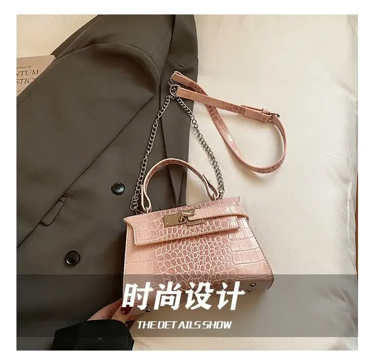 Pink faux leather crossbody diaper bag with crocodile texture, metal chain, and adjustable strap for carrying baby gear.