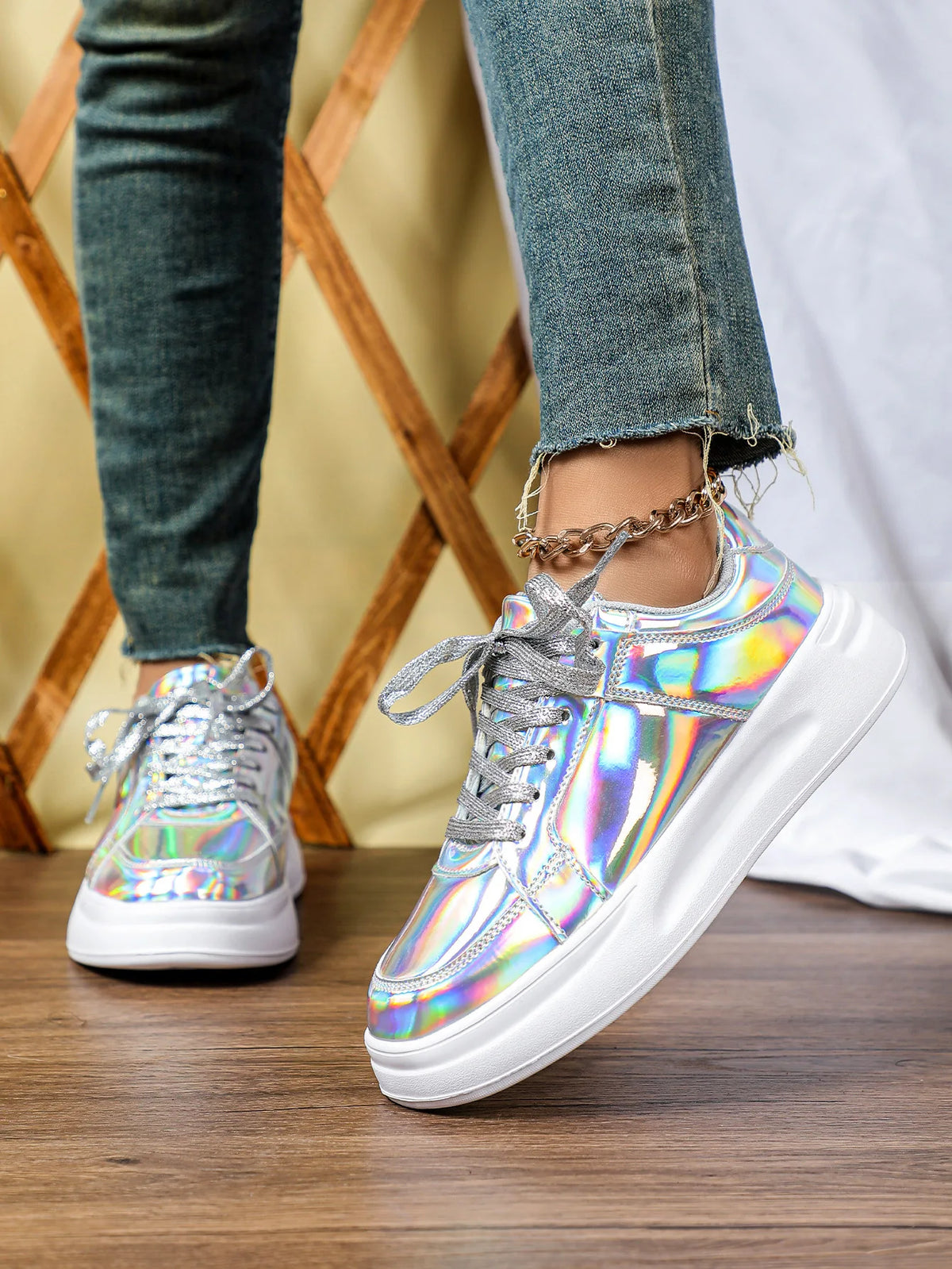 Silver iridescent chunky sneakers with metallic laces and thick white soles, worn with jeans.