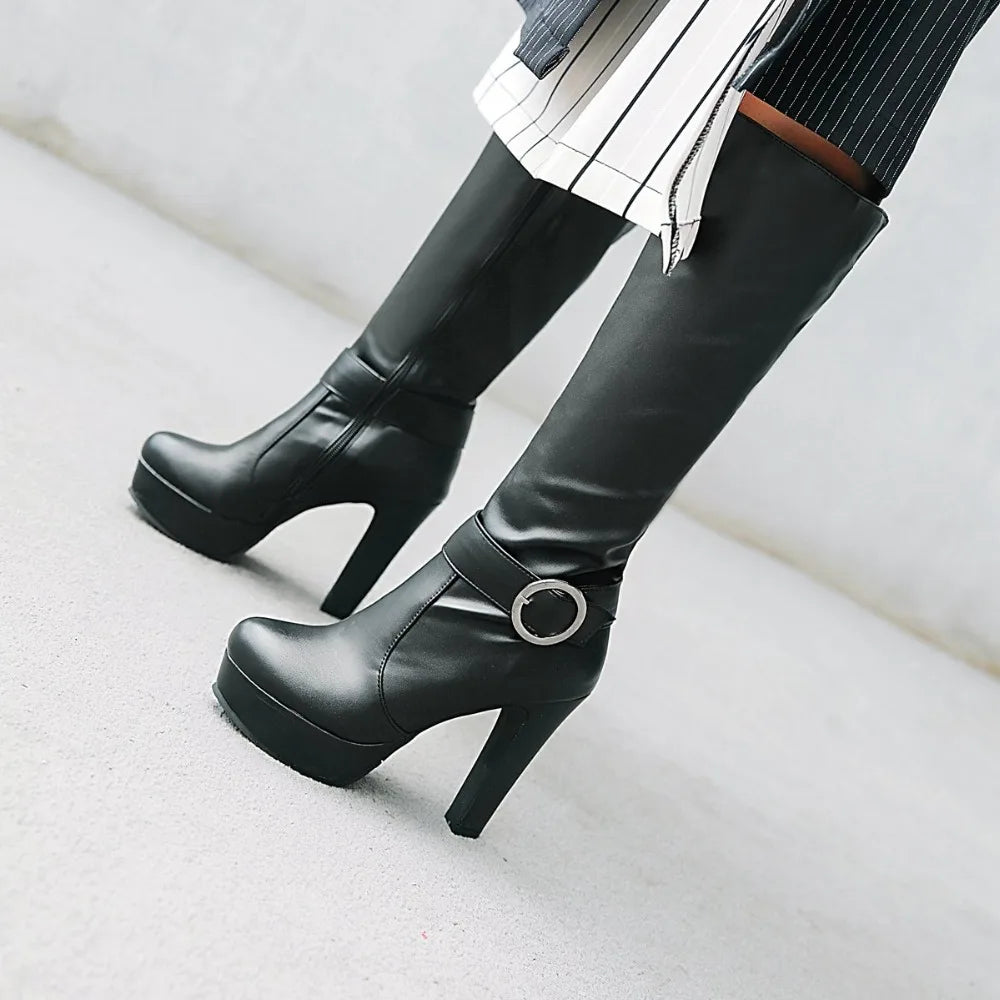 Black faux-leather knee-high platform boots with high block heels and a side buckle strap detail.