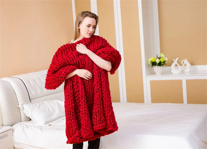 Chunky red hand-knitted yarn blanket draped over a woman's shoulders inside a bedroom.