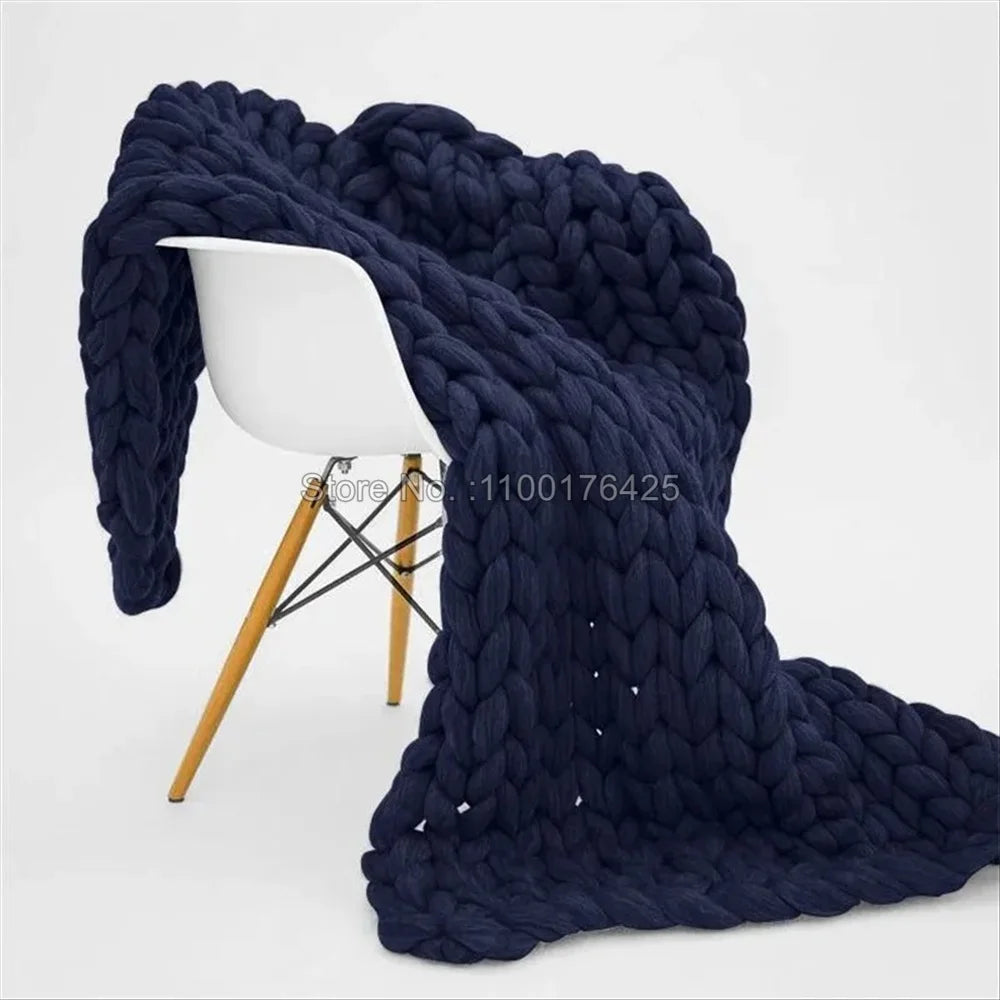 Dark blue chunky knit blanket draped over a modern white chair with wooden legs.