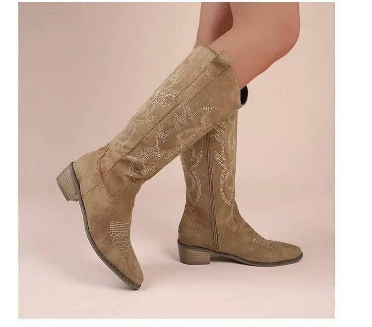 Tan faux suede tall western cowboy boots featuring ornate white stitching, pointed toes, and block heels.