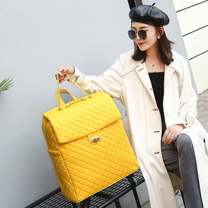 A person holds a yellow quilted PU leather rolling suitcase with a chain handle and twist-lock closure.
