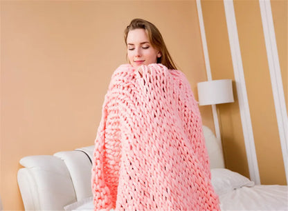A pink chunky knit blanket wrapped around a woman standing in a bedroom.