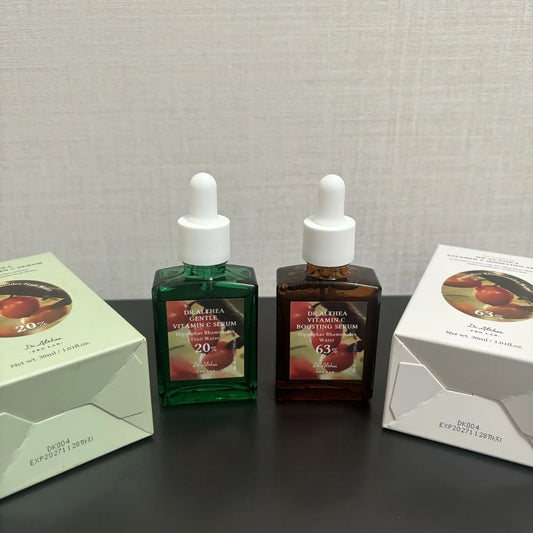 Two dropper bottles of vitamin c serum with green and brown glass alongside their matching boxes.