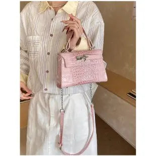 Light pink faux leather structured diaper bag with crocodile texture and adjustable strap for carrying baby essentials.