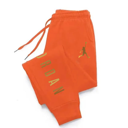 Orange midweight joggers with gold lettering, drawstring waist, and stretchy fabric for athletic wear.