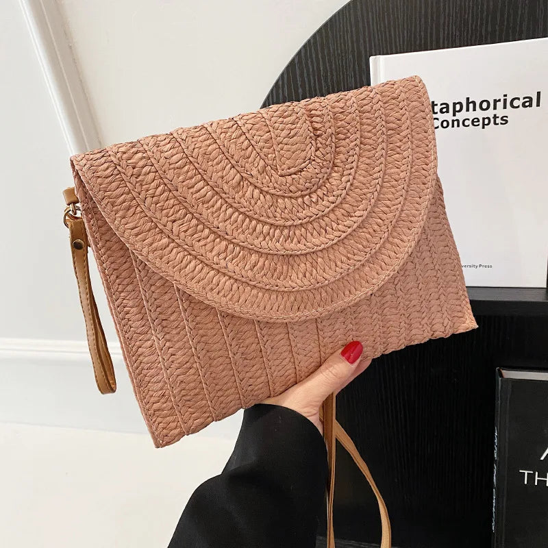 Tan straw woven crossbody bag with a curved flap and adjustable strap for beach outings.